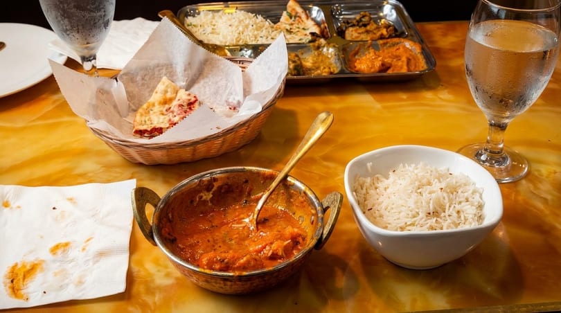 Indian food on a table, including naan, rice, curry, and a thali platter.