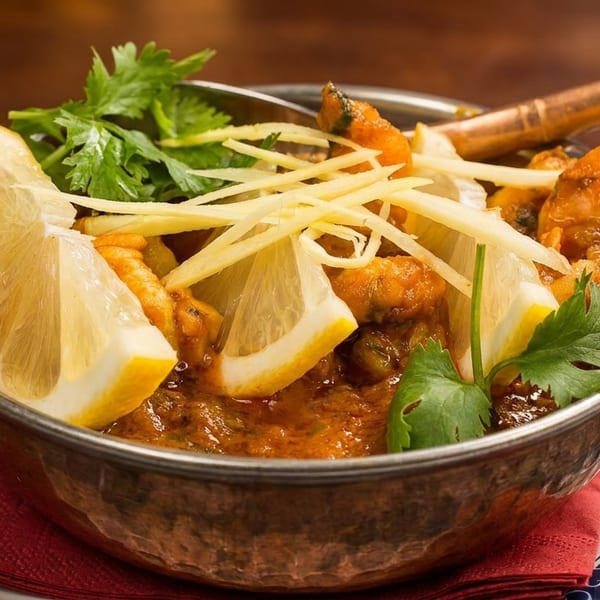 Indian curry in a copper bowl, garnished with lemon wedges, ginger strips, and cilantro.