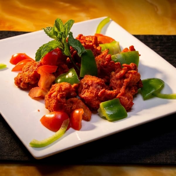Spicy red chicken pieces with green bell peppers, tomatoes, and mint on a white plate.