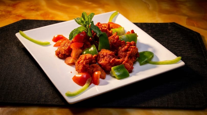 Spicy red chicken pieces with green bell peppers, cherry tomatoes, and mint on a white plate.